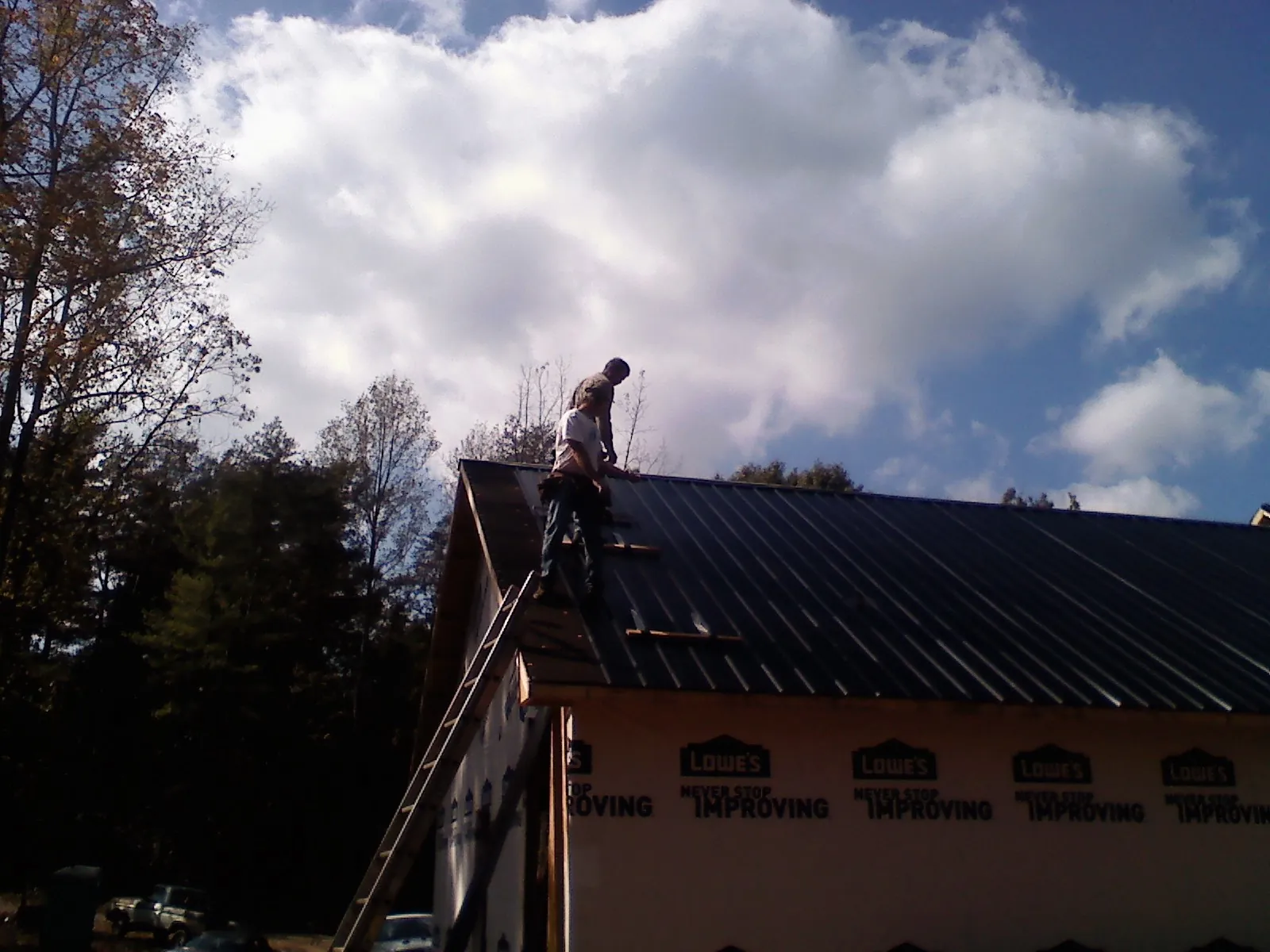 Roofer fastening dark metal panels high against a cloudy sky, from a Roof Inspection job in Helena