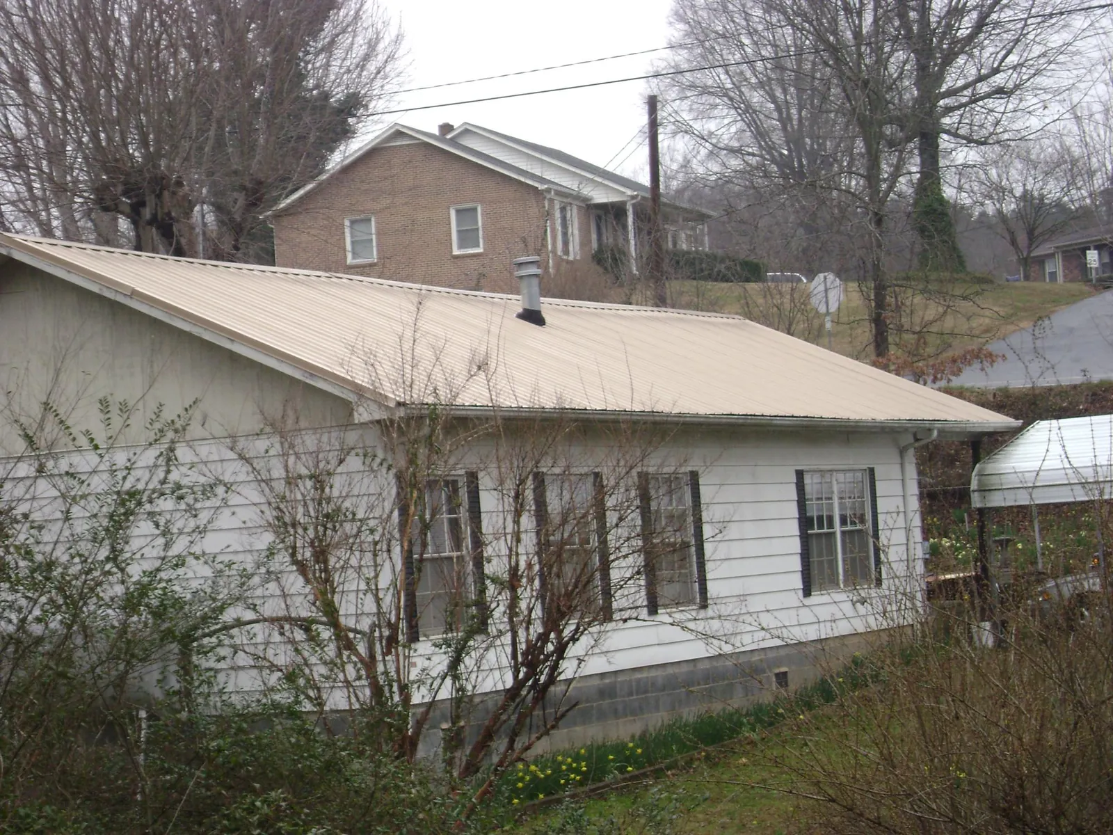 Tan metal roof on a white sided house set into a hillside — Commercial Roofing by Roofing Brothers in Helena